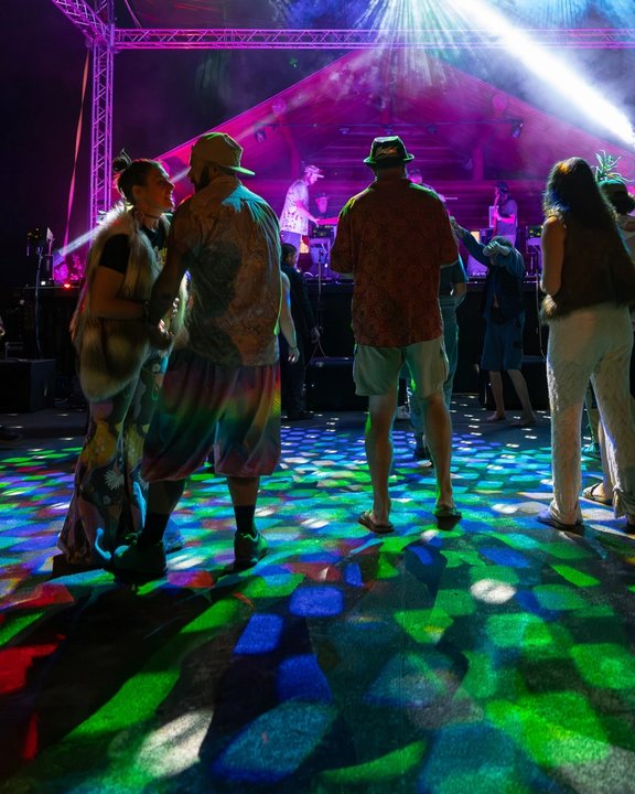 Festival attendees dancing beneath colorful nighttime lights