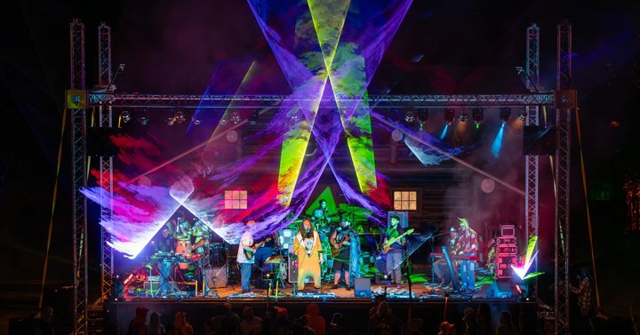 Live band beneath colorful lasers and geometric stage decorations