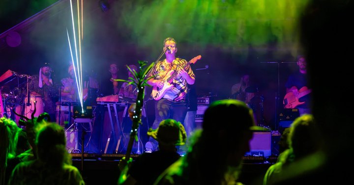 Guitarist performing beneath green and purple stage lights