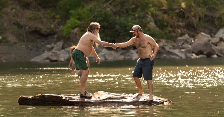Two festival attendees balancing together on a log in the river