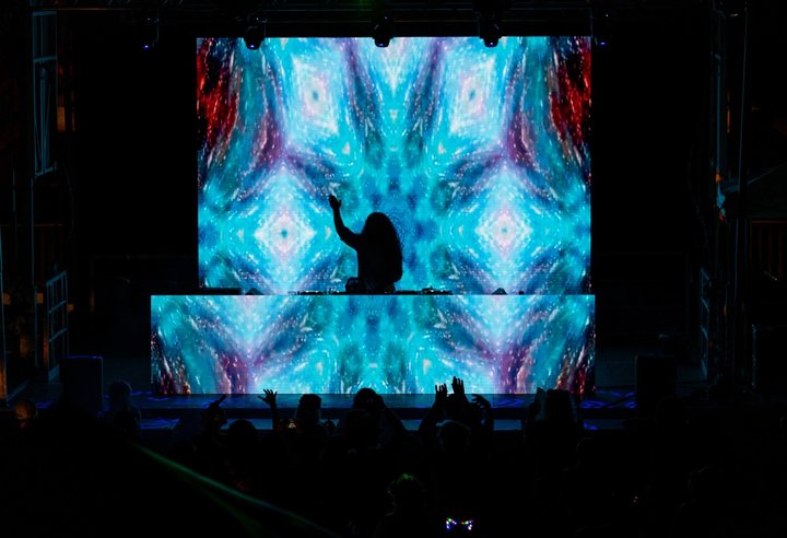 Festival crowd watching a DJ with a large blue visual backdrop
